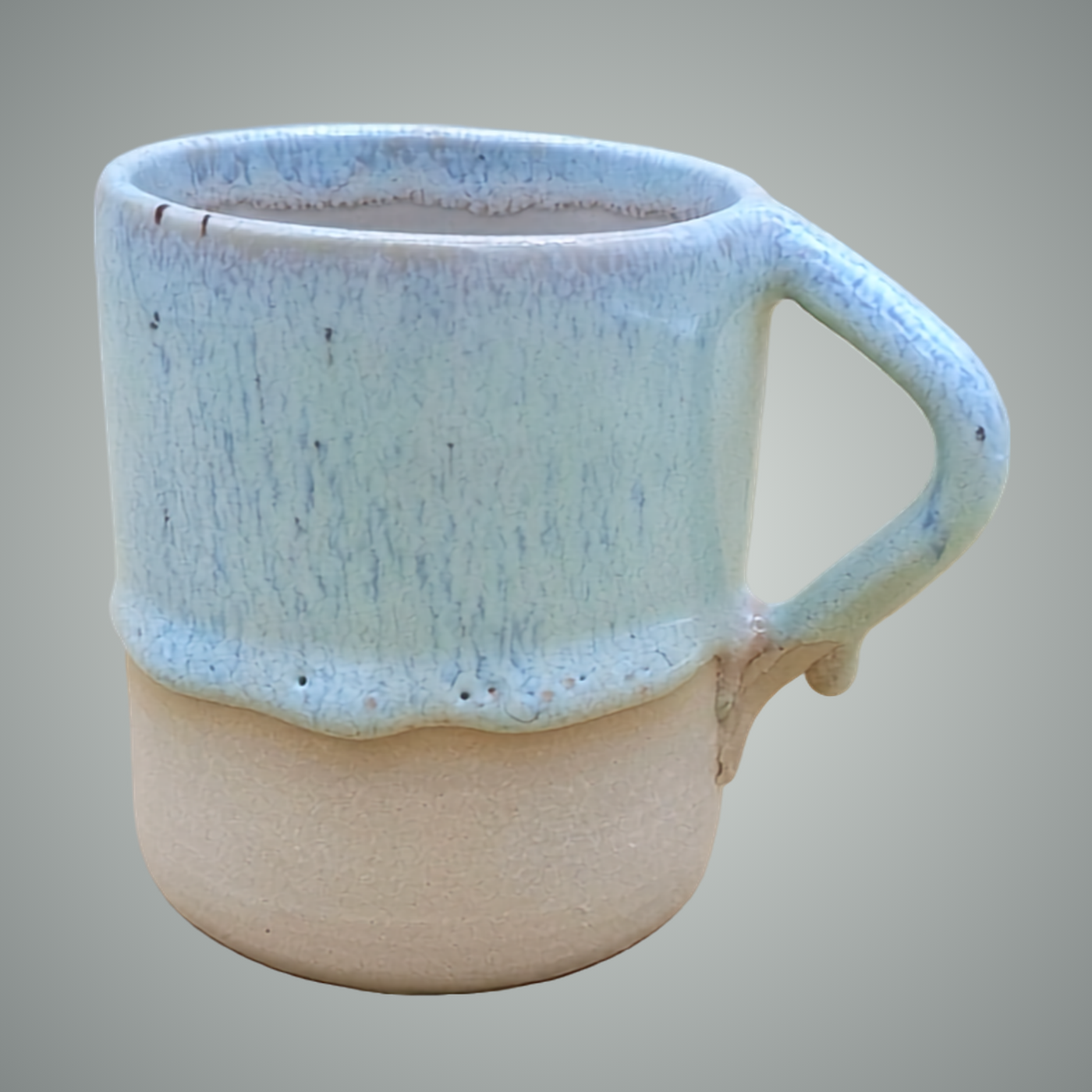 Handmade wheel-thrown stoneware cup with soft blue drip glaze and unglazed base. Geometric angular handle. One of a kind by ceramist Przemysław Gołębiewski, Berlin.